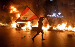 Un manifestante con la bandera libanesa corre mientras bloquean la carretera Jounieh-Trípoli con neumáticos en llamas, Beirut, 11 de junio de 2020.