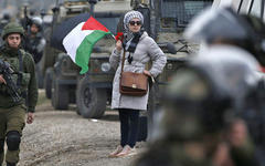 Una mujer palestina con la bandera nacional se encuentra junto a los soldados israelíes durante una manifestación contra los asentamientos israelíes en la aldea de Qusra, en la Cisjordania ocupada por Israel el 2 de marzo (AFP)