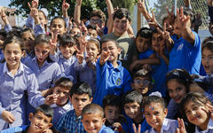 Niñas y niños que asisten a las escuelas de UNRWA en el campamento de refugiados de Jalazone Palestina en Cisjordania saludan durante un recreo | Foto: Marwan Baghdadi (© 2018 UNRWA)