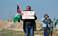 Palestino lleva un cartel que dice "Israel es un estado de apartheid", Cisjordania ocupada, 2019. Foto: AFP. 